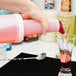 A person pouring a drink from a white Carlisle Store 'N Pour bottle into a glass.