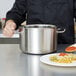 A person holding a Vollrath silver sauce pot with a plate of pasta.