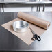 A roll of Baker's Mark PanPal non-stick pan liner paper on a table with a silver bowl.