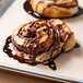 A close up of a chocolate and caramel swirl cinnamon roll on a Baker's Mark PanPal pan liner.