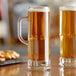 Two Libbey Frankfurt beer tasting mugs filled with yellow liquid on a table in a bar.