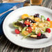 A Tuxton Colorado bright white narrow rim china plate with a salad on it, with a fork.