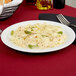 A Tuxton Colorado narrow rim bright white china plate with a fork and a plate of pasta with asparagus, chicken, and vegetables.