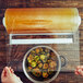 A person using a Bulman white plastic wrap dispenser to cover a container of food on a table.