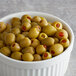 A close up of a bowl of green olives with red and green peppers.