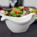 A white sauce in a Tuxton white china gravy boat.