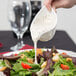A person using a Tuxton white china gravy boat to pour white liquid over a salad.