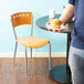 A person sitting in a Lancaster Table & Seating cafe chair at a table holding a plate of muffins.