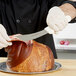 A person holding a Dexter-Russell beef skinning knife over a piece of meat on a plate.