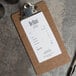 A dark brown Menu Solutions clipboard with a paper and pen on it.