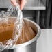 A hand using a plastic liner to cover a pot of food.