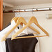 A closet with clothes hanging on Winco maple wood hangers.