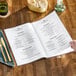 A person holding a clear menu on a brown table.