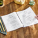 A person reading a H. Risch, Inc. clear heat sealed menu cover on a table.