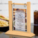 A Menu Solutions natural wood flip top table tent on a table.