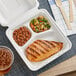 A white EcoChoice takeout box with 3 compartments holding grilled chicken, beans, and a drink.