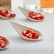 A white compostable plant fiber taster spoon filled with a small serving of diced tomatoes and herbs.