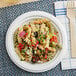 A plate of pasta salad with a fork on a EcoChoice Compostable Sugarcane plate.