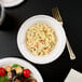 A bowl of macaroni and cheese on a white background with a salad and a glass of wine.