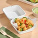 A white plant fiber take-out container filled with tater tots and sliced peppers.