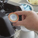 A person's hand holding a Caffe de Aroma Decaf French Vanilla Coffee single serve cup with a lid.