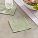 A green Choice Sage 2-Ply beverage napkin on a table with a bowl of flowers.