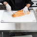 A person cutting bread with a knife on a San Jamar white cutting board.