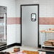 A single aluminum swinging traffic door with a small rectangular window, installed in a commercial kitchen setting.