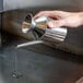 A hand pouring liquid from a Town stainless steel oil dispenser.