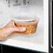 A hand holding a Pactiv translucent round deli container of food in a microwave.