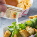 A person pouring Italian dressing onto a salad.