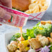 A person using a Thousand Island dressing packet to pour dressing over a salad.