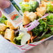 A hand holding a Ranch dressing packet and pouring it onto a salad.