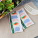 Two packets of ranch dressing on a table with a bowl of salad and a plastic fork.