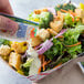 A hand holding a Ranch dressing packet over a salad on a counter.