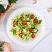 A Dart white foam plate with a salad of tomatoes, avocado, and lettuce.