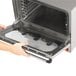 A hand opening a Vollrath convection oven door over a pan.