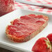 A slice of bread with strawberry jam on it on a table.