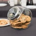 An Anchor Hocking glass penny candy jar filled with cookies on a table.