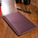 A Tablecraft burgundy vinyl server book with a wood surface.