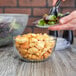 A hand holding a plate of salad in front of an Anchor Hocking glass bowl.