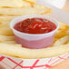 A Solo translucent polystyrene souffle cup of ketchup on french fries.