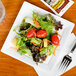 A WNA Comet white square plastic salad plate with salad, tomatoes, lettuce and carrots.