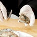 A person in gloves using a Tablecraft Frenchman Style FirmGrip handheld oyster knife to open an oyster.