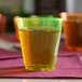A Fineline Quenchers neon yellow hard plastic shot cup filled with green liquid on a table.