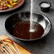 A bowl of brown liquid with a spoon and a whisk on a table.