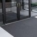 A gray unbacked Cactus Mat with a coil pattern used outside a building with glass doors.