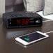 A black Conair digital alarm clock with a cell phone charging on it.