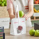 A woman holding a green apple in a white paper bag with a picture of apples.