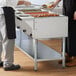 A four pan electric steam table with an undershelf, designed for keeping food warm in a buffet or cafeteria setting.